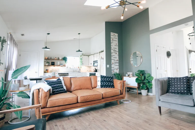 Tan leather sofa with black-and-white cushions, a white throw and green houseplants in an open-plan living room.