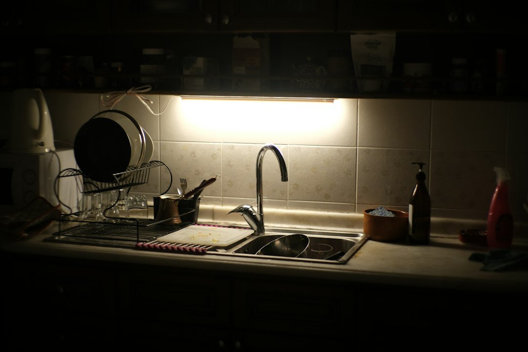 Kitchen sink area lit by under-cabinet lighting in the evening