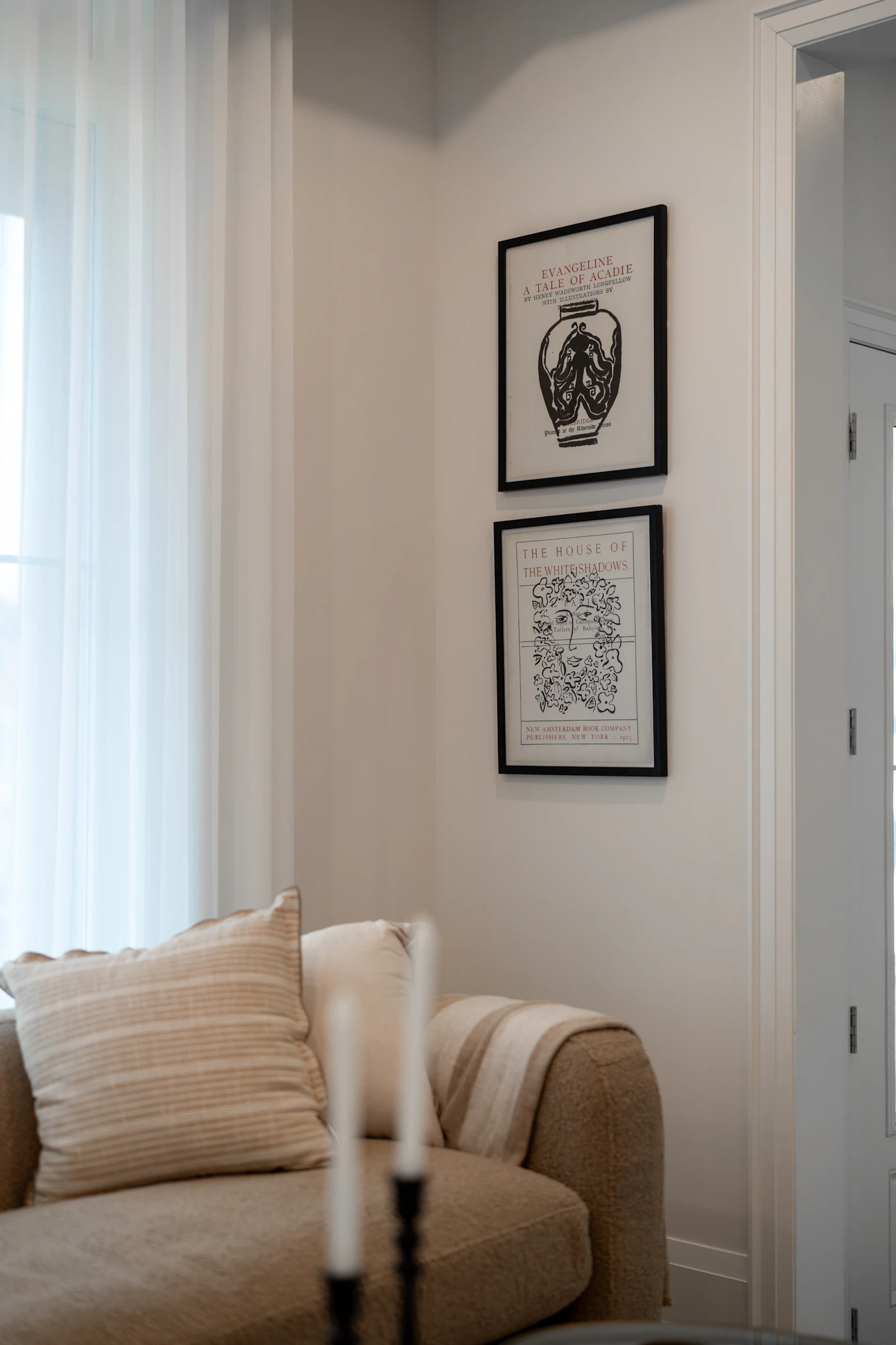 Two black-framed vintage book-cover prints stacked vertically on a pale wall beside a cream sofa.